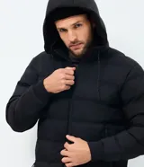 Campera puffer deportiva color verde militar, sin costuras, con capucha ajustable por cordón, bolsillos laterales con cierre y cierre frontal por cremallera.