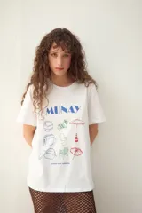 Remerón blanco oversize de algodón, con estampado frontal de estilo playero que incluye un cocodrilo, un paraguas de playa, una silla de playa y otros elementos.