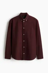 Camisa H&M de manga larga, color bordó, confeccionada en algodón Oxford. Presenta cuello americano, cierre frontal con botones, un bolsillo en el pecho y dobladillo redondeado.
