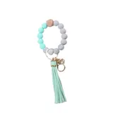 Llavero con pulsera de cuentas redondas de silicona en tonos celeste y gris, con un cubo de madera natural y borla decorativa en color celeste.