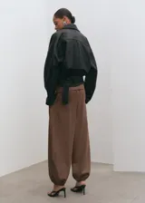 Pantalón balloon de tiro alto color marrón, confeccionado en algodón, con cintura ajustable con elástico, pinzas en la parte delantera, bolsillos laterales y bajos fruncidos con elástico.