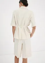 Short de mezcla de lino color beige con sutiles rayas verticales, diseño recto y tiro medio, con bolsillos laterales y trabillas para cinturón.
