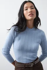 Polera de tejido de punto con textura calada y diseño de líneas verticales acanaladas. Presenta cuello alto y mangas largas con puños delicados, de silueta entallada.