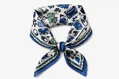 Pañuelo cuadrado de seda con estampado de accesorios de viaje y bolsos en tonos azules, verdes y negros sobre fondo blanco. Presenta un borde con franjas decorativas en azul y verde.