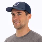 Gorra tipo trucker color azul, con panel frontal y visera de tela técnica, y paneles laterales y traseros de malla transpirable. Presenta un parche circular bordado en el frente con el logo de Merrell y un diseño de montaña.