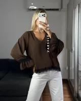 Blusa de tela cey color bordó, con escote en V y mangas largas abullonadas que terminan en puños con detalle de encaje y volados.