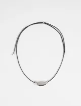 Collar de cordón negro con dije metálico de forma curva y acabado plateado.