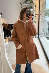 Campera de cuero genuino color marrón con interior de corderito sintético, capucha, bolsillos frontales aplicados y cierre de tipo duffel con cordones y botones alargados.