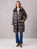 Campera puffer larga de acabado satinado en tono beige. Presenta un diseño capitoneado horizontal, cierre frontal bidireccional y un amplio cuello envolvente revestido en piel sintética. Incluye bolsillos laterales funcionales con cierre y logo metálico en la manga.