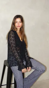 Blusa de encaje negro con escote en V, cierre frontal con lazos y mangas largas con terminación acampanada.