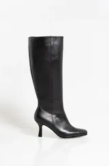 Botas altas de cuero negro con caña media, punta fina y taco aguja de 6 cm. Diseño minimalista de líneas limpias y silueta estilizada.