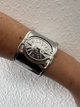Brazalete ancho plateado con diseño de sol con rostro en el centro.