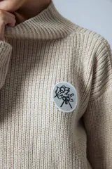 Sweater de punto grueso color crema, con cuello alto y parche circular con bordado en el pecho.