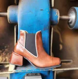 Bota tipo chelsea de cuero color óxido, con elástico lateral negro y ribetes en color crema. Presenta un taco cuadrado robusto y punta cuadrada.
