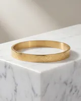 Pulsera tipo esclava rígida de acero con baño de oro, con diseño grabado de patrón geométrico de rombos en toda su superficie.