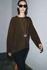 Blusa de cuello redondo y manga larga, confeccionada en tejido fluido con acabado satinado. Presenta un diseño de corte holgado, bajo recto y cierre en la espalda mediante una pequeña abertura con botón.