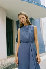 Vestido midi de color azul, confeccionado con lino. Presenta cuello redondo, manga sisa y diseño sin mangas. Cuenta con bajo asimétrico y detalle de vuelo en la parte frontal.