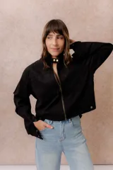 Chaqueta de gamuza sintética color negro, de calce relajado y largo a la cintura. Presenta cuello mao con cierre a presión, cierre frontal metálico, bolsillos delanteros de placa y puños con broche regulable.