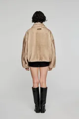 Campera corta de pelo sintético en color beige, con diseño de volumen amplio, cuello clásico, cierre frontal con cremallera y bolsillos laterales integrados.