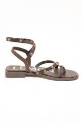 Sandalias planas de cuero marrón, con tiras finas decoradas con tachas metálicas redondas y tira ajustable alrededor del tobillo.