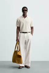 Polo negro de manga corta con cuello solapa y abertura frontal. Presenta un tejido jacquard con textura geométrica sutil.