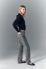 Jean de tiro alto confeccionado en denim rígido de color gris con lavado localizado. Presenta un corte de pierna recta y un detalle de apliques brillantes a lo largo de las costuras laterales.