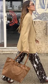 Cartera tipo tote de símil gamuza color marrón, con diseño estructurado y amplio, asas de hombro delgadas y detalle de tira con hebilla y argollas metálicas en la parte superior.