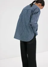 Camisa oversize de algodón estilo denim, de color azul con estampado de rayas, cuello camisero, manga larga con puños abotonados, bolsillo de parche en el pecho y cierre frontal con botones.