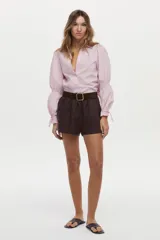 Camisa blanca de manga larga abullonada con detalle de punto smock en los puños y cordones para atar. Presenta cuello clásico y cierre frontal de botones.