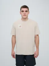 Remera de manga corta color beige, con cuello redondo y diseño holgado. Cuenta con un pequeño estampado rectangular en el pecho con motivo futbolero.