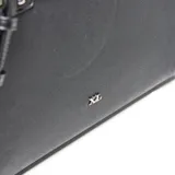 Cartera tipo tote de cuero sintético negro con textura granulada. Presenta doble asa superior, correa ajustable extraíble y detalle de tira decorativa con cierre metálico frontal. Incluye logo metálico de la marca en la parte inferior.