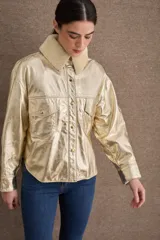 Campera de cuero metalizado color dorado con cuello de corderito sintético en tono crema. Presenta cierre frontal con botones metálicos, bolsillos frontales con solapa y diseño de corte recto.