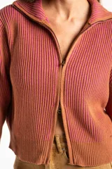 Campera tejida de algodón con diseño acanalado, cuello alto y cierre frontal completo. Presenta un patrón bicolor en tonos terracota y rosado, con puños y cintura elásticos.