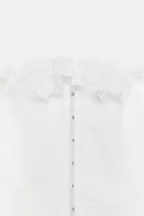 Top corsetero blanco con escote cuadrado y tirantes anchos con volados de encaje. Presenta costuras marcadas y cierre frontal con ganchos metálicos.