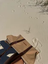 Bolso tote color beige con asas de cuero marrón, cierre superior y bolsillo interno.