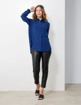 Camisa de satén color violeta, con cuello clásico, cierre frontal con botones, manga larga con puños anchos abotonados y bolsillo aplicado en el pecho.