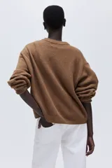 Buzo de punto color marrón, de manga larga con cuello redondo, hombros caídos y puños y bajo acanalados.