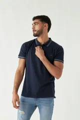 Remera polo azul marino de manga corta, con cuello y puños acanalados con rayas grises. Presenta un logo estampado en el pecho.
