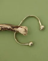 Brazalete rígido abierto de metal color plateado, con terminaciones en forma de herradura.