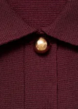 Chaqueta de punto de corte recto y diseño cropped, color bordó. Presenta cuello camisero, cierre frontal con botones dorados, mangas largas y dos bolsillos de parche con solapa en el pecho.