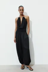 Body negro de cuello halter con detalle de pieza metálica y aplicación joya. Escote pico pronunciado y tejido drapeado. Cierre en bajo con botones a presión.