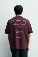 Camiseta de corte relajado color bordó, con cuello redondo y manga corta. Presenta un pequeño texto bordado en contraste en el pecho.