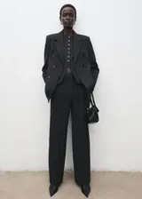 Pantalón de traje de tiro medio, color negro, de diseño recto y largo, con cierre frontal de cremallera, botón y ganchos ocultos con tapeta, y bolsillos laterales.