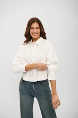 Camisa de corte cropped y diseño holgado, color blanco, con cuello clásico, cierre frontal de botones y mangas largas con puños anchos.