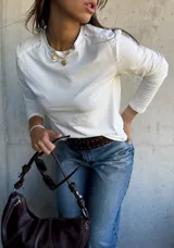 Remera de manga larga color blanco, con cuello redondo y detalle de tachas metálicas en los hombros.