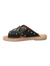 Sandalia tipo ojota con base de yute, tiras cruzadas de cuero negro con tachas doradas y hebilla metálica decorativa.