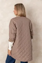 Campera acolchada de corte amplio y largo midi, color beige con diseño capitoneado. Presenta mangas tres cuartos con puños vueltos que revelan un interior estampado con motivo animal print. Diseño sin cuello y cierre frontal oculto.