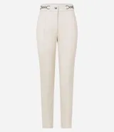 Pantalón legging color beige con frente de poliuretano que imita cuero y parte trasera de punto roma. Presenta detalle de cadena metálica en la cintura y cierre frontal.