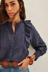 Camisa de algodón azul marino con diseño texturizado, cuello mao y volados frontales. Presenta mangas largas con puños ajustados y detalles de encaje en los bordes.