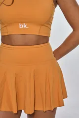 Conjunto deportivo compuesto por un top de escote redondo con logo estampado y una pollera short con tablas. Diseño en color naranja, confeccionado en tejido elástico de secado rápido.